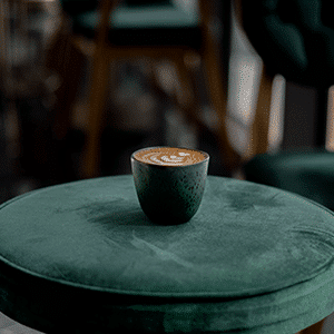latte in a green mug sitting on a velvet green stool